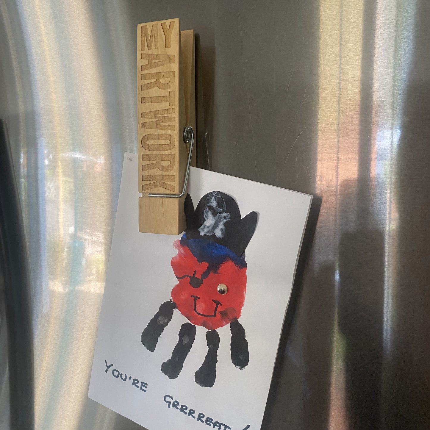 A child’s drawing held up on a fridge with a Jumbo Peg, keeping the artwork visible and secure.