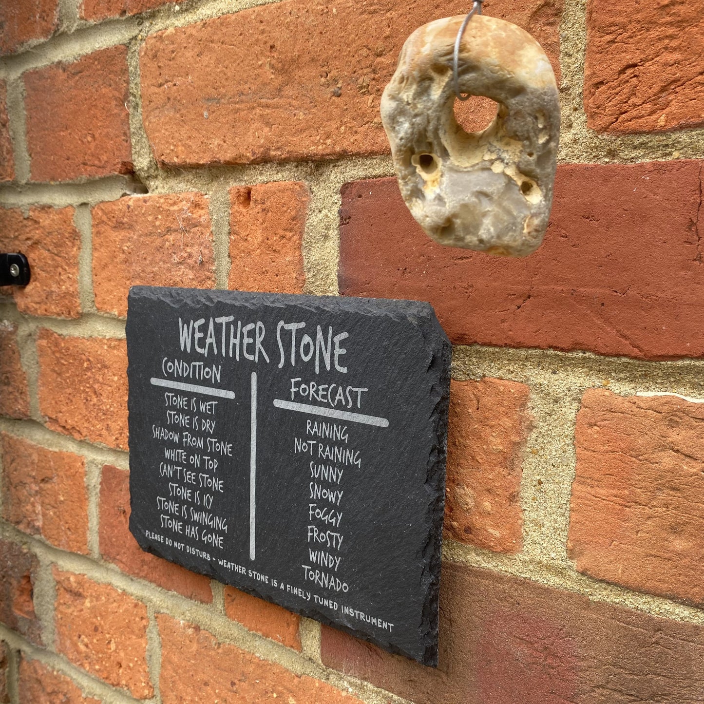 Slate sign with hanging hag stone for quirky weather prediction, displayed outdoors