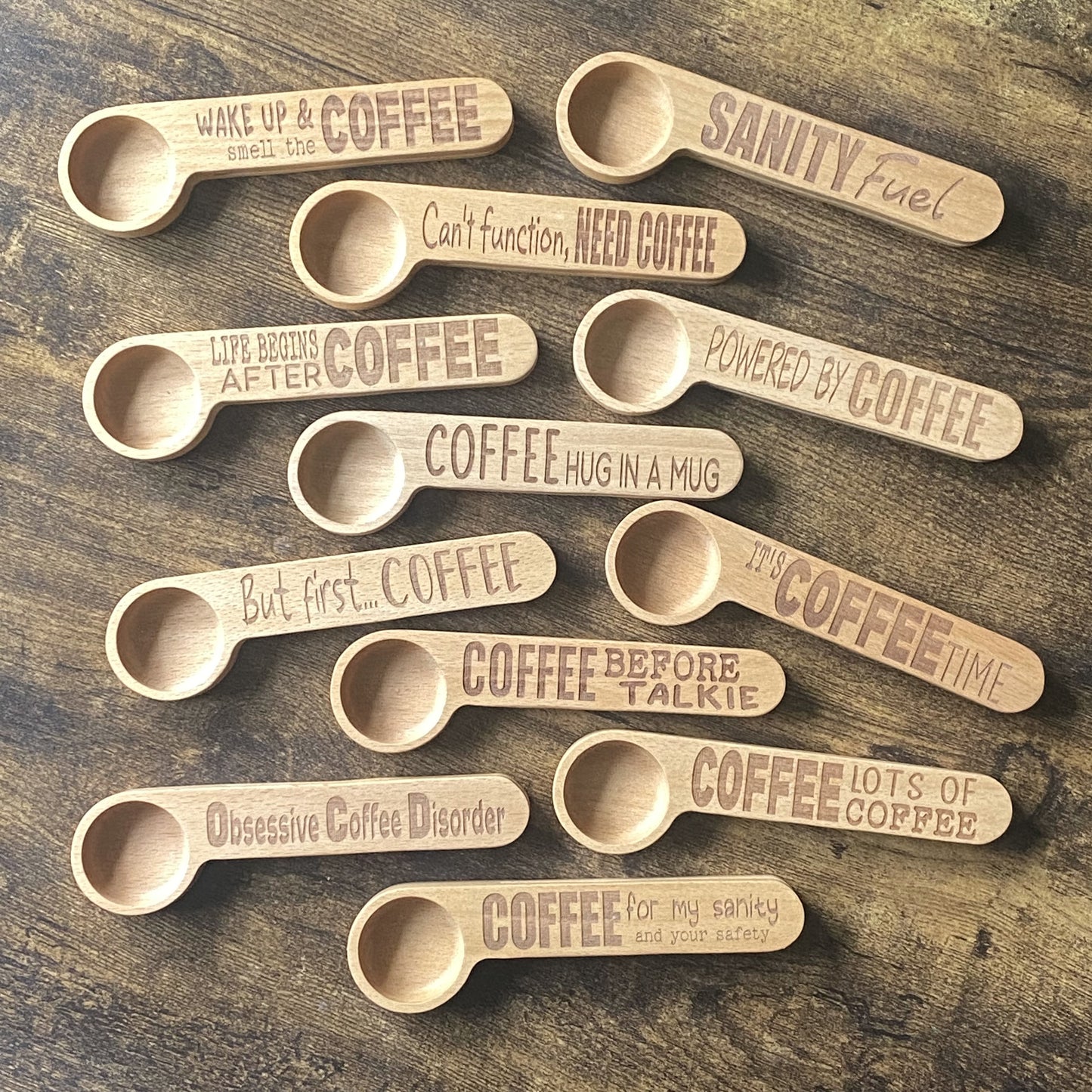 A top-down view of a selection of wooden coffee spoons, each engraved with different witty coffee quotes, arranged to showcase the unique designs.