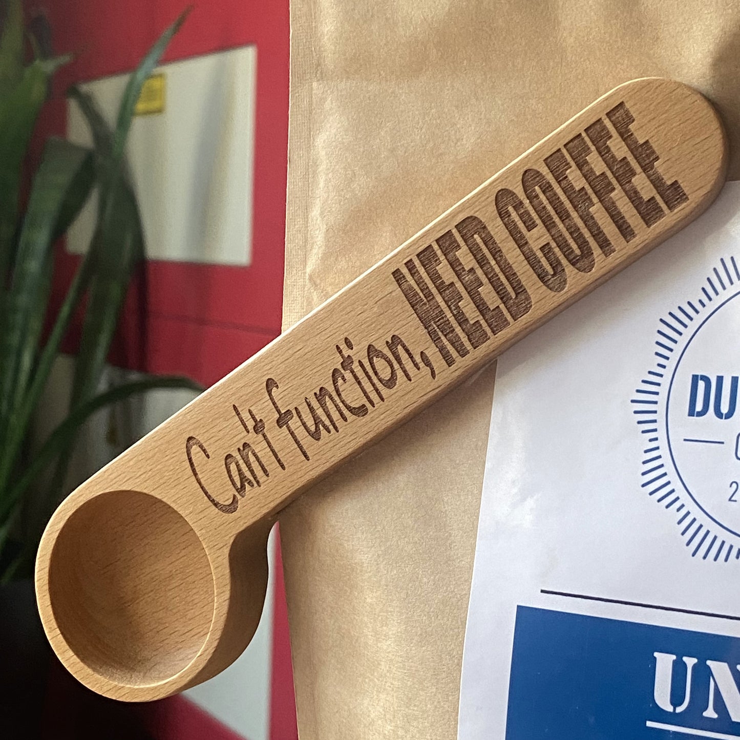 Wooden coffee scoop clipped onto a coffee bean bag, set in a studio environment, showcasing the practical design and engraved details.