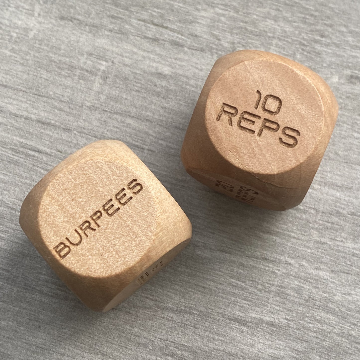 Top-down view of Adult Exercise Decision Dice pair, showing full-body exercise engravings on solid wood