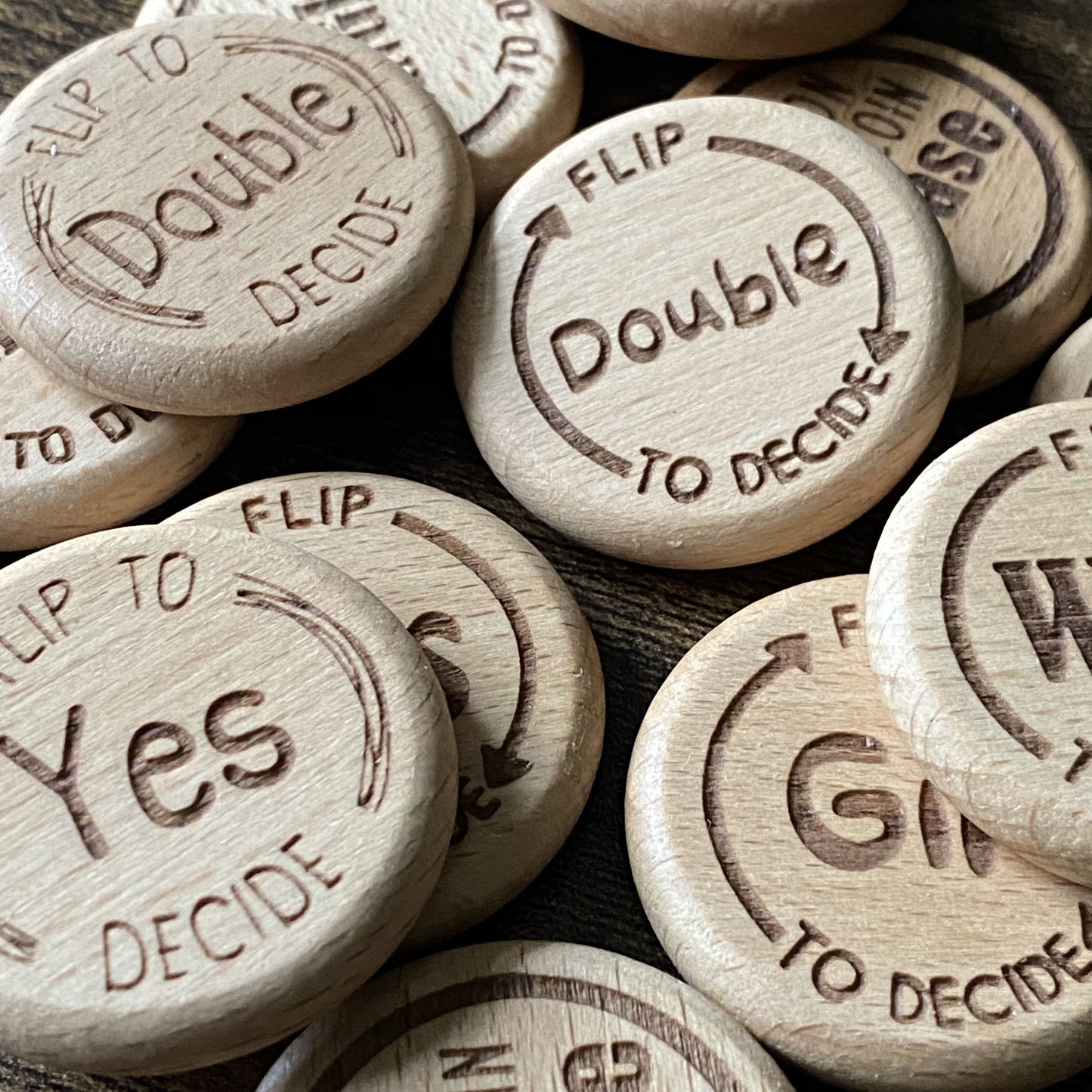 Mixed pile of Friday Night Drinking Trio Flip Coins in all four designs, showcasing the variety of engraved wooden styles