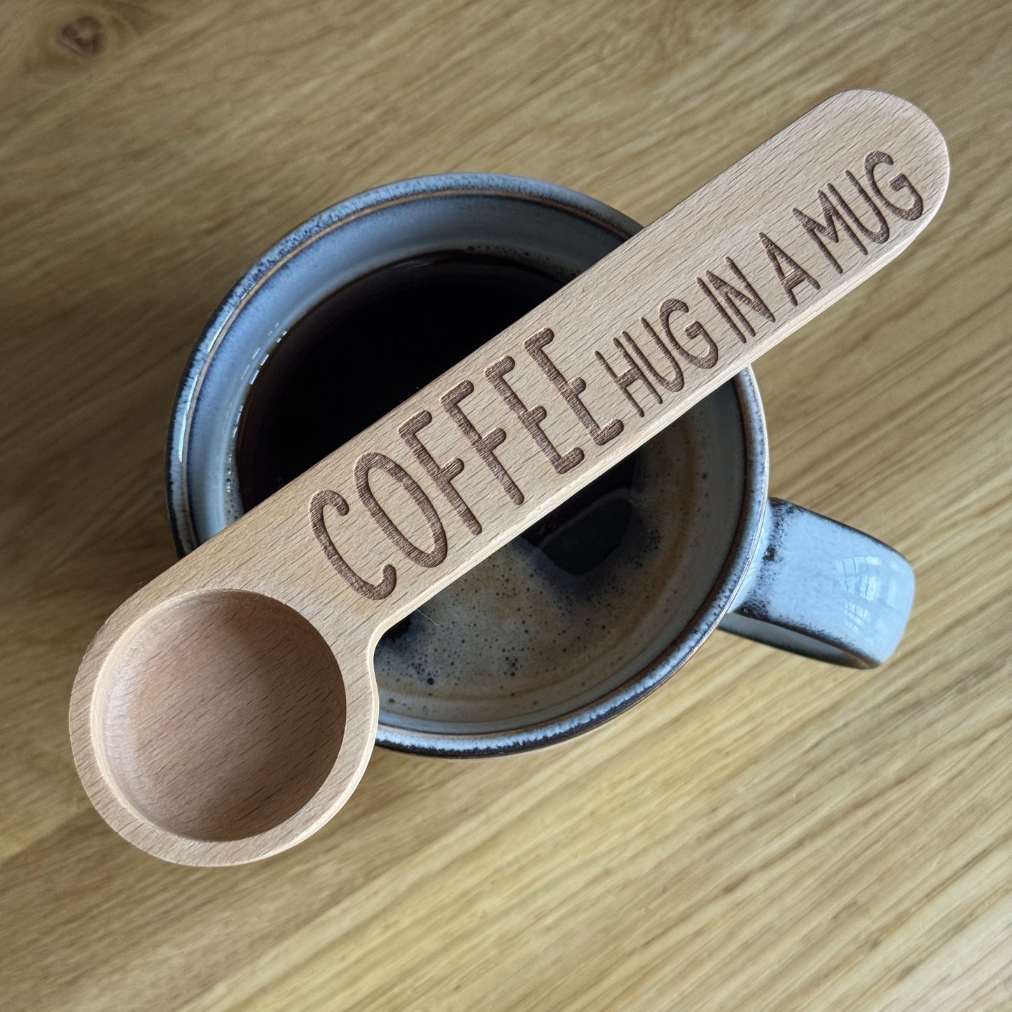 Top-down view of a mug with a Hug in a Mug engraved coffee spoon resting across the top