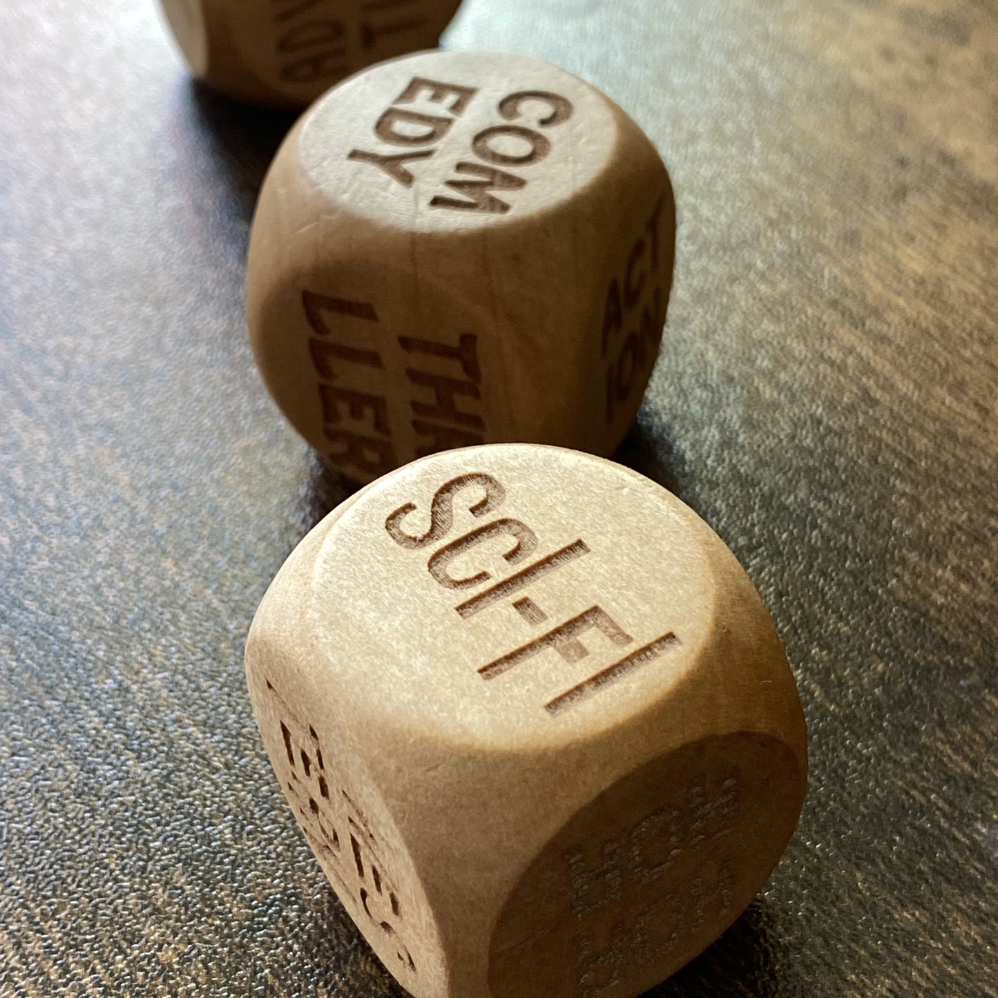 Angled close-up of Movie Night Decision Dice showing the engraved word “Comedy” and "Sci-Fi" in focus with other genres subtly visible in background
