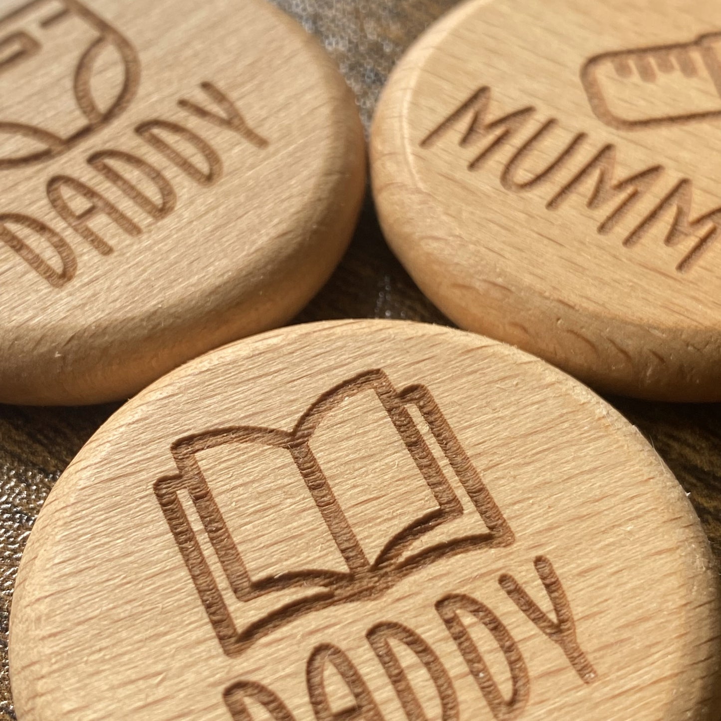Close-up of the solid wood New Baby Duties Flip Coins, highlighting their tactile texture and engraved wording combinations