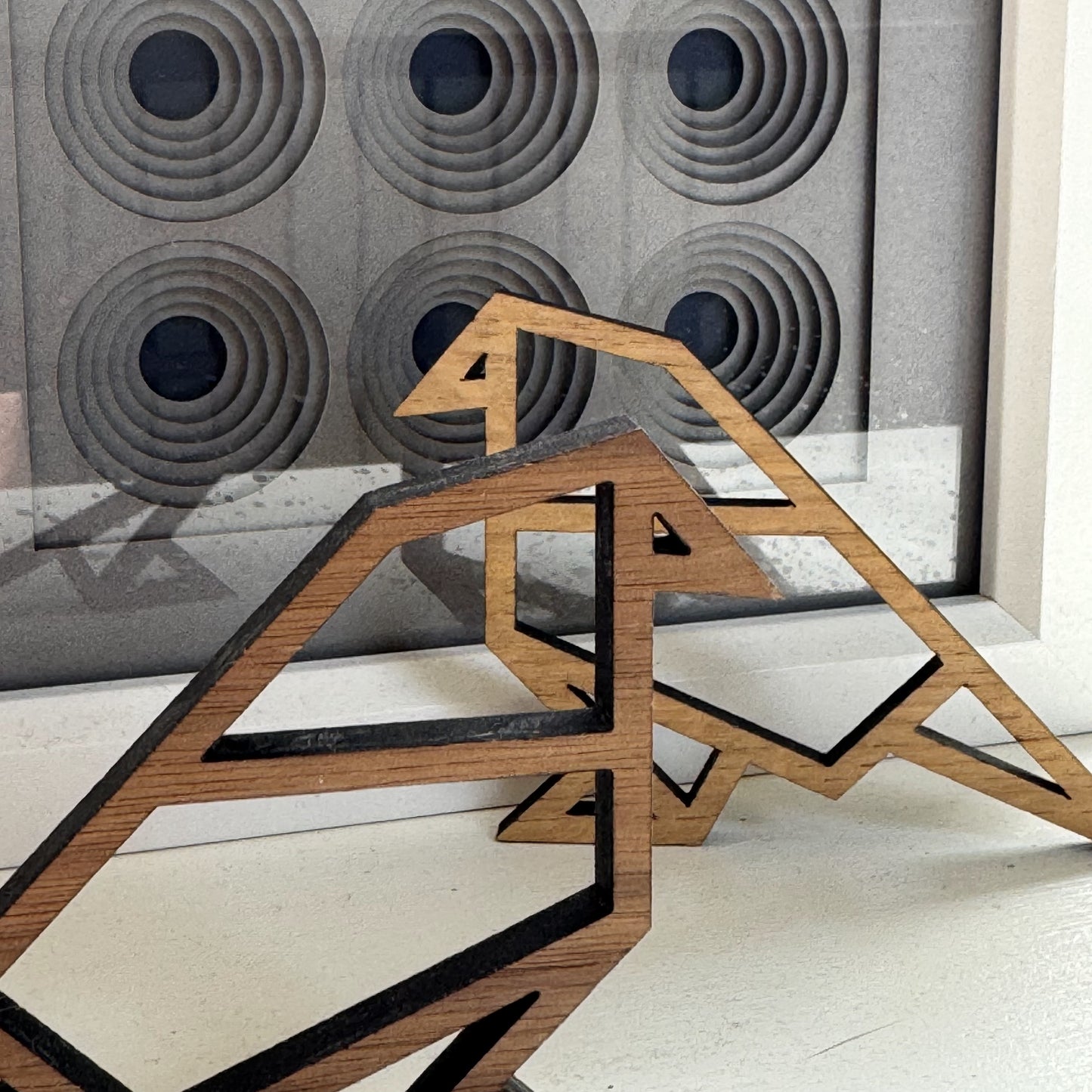 Wooden bird ornaments in front of geometric papercut artwork – origami-inspired modern wall display