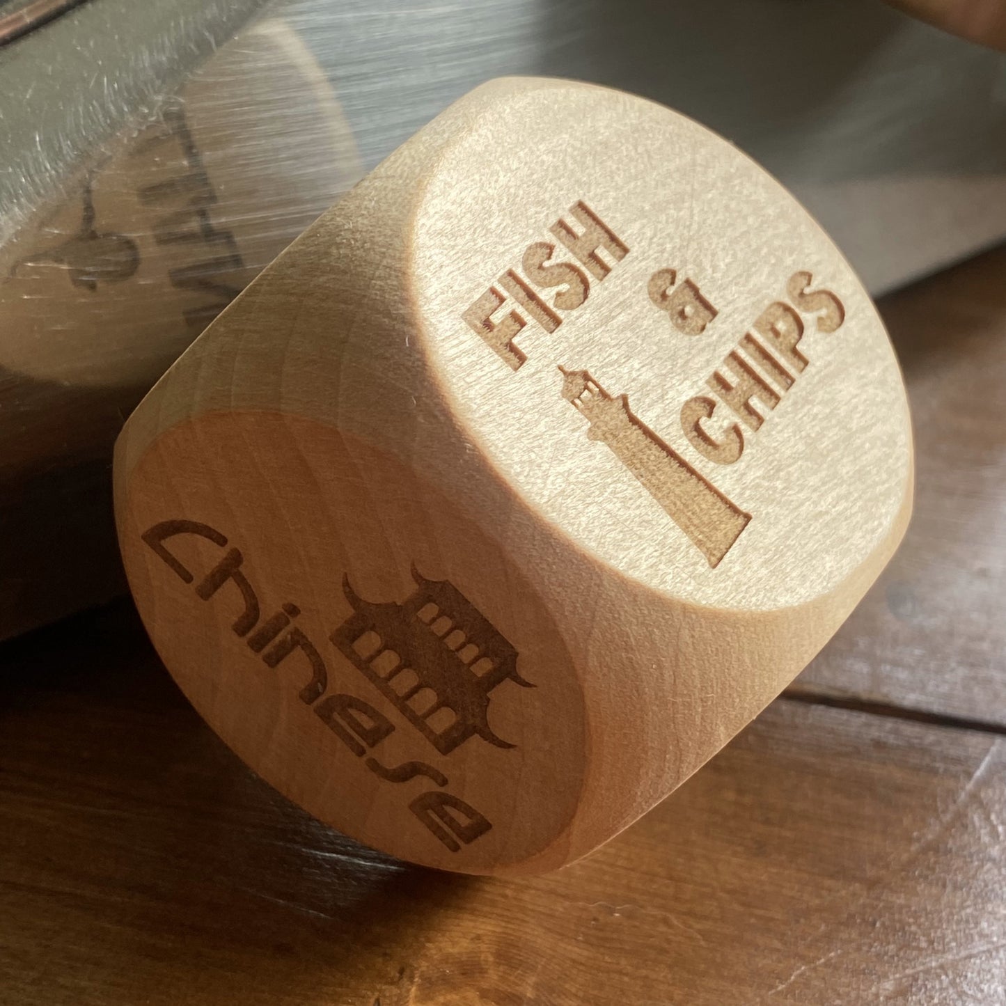 Angled shot of Takeout Decision Dice with 'Fish & Chips' engraving on a home wooden table