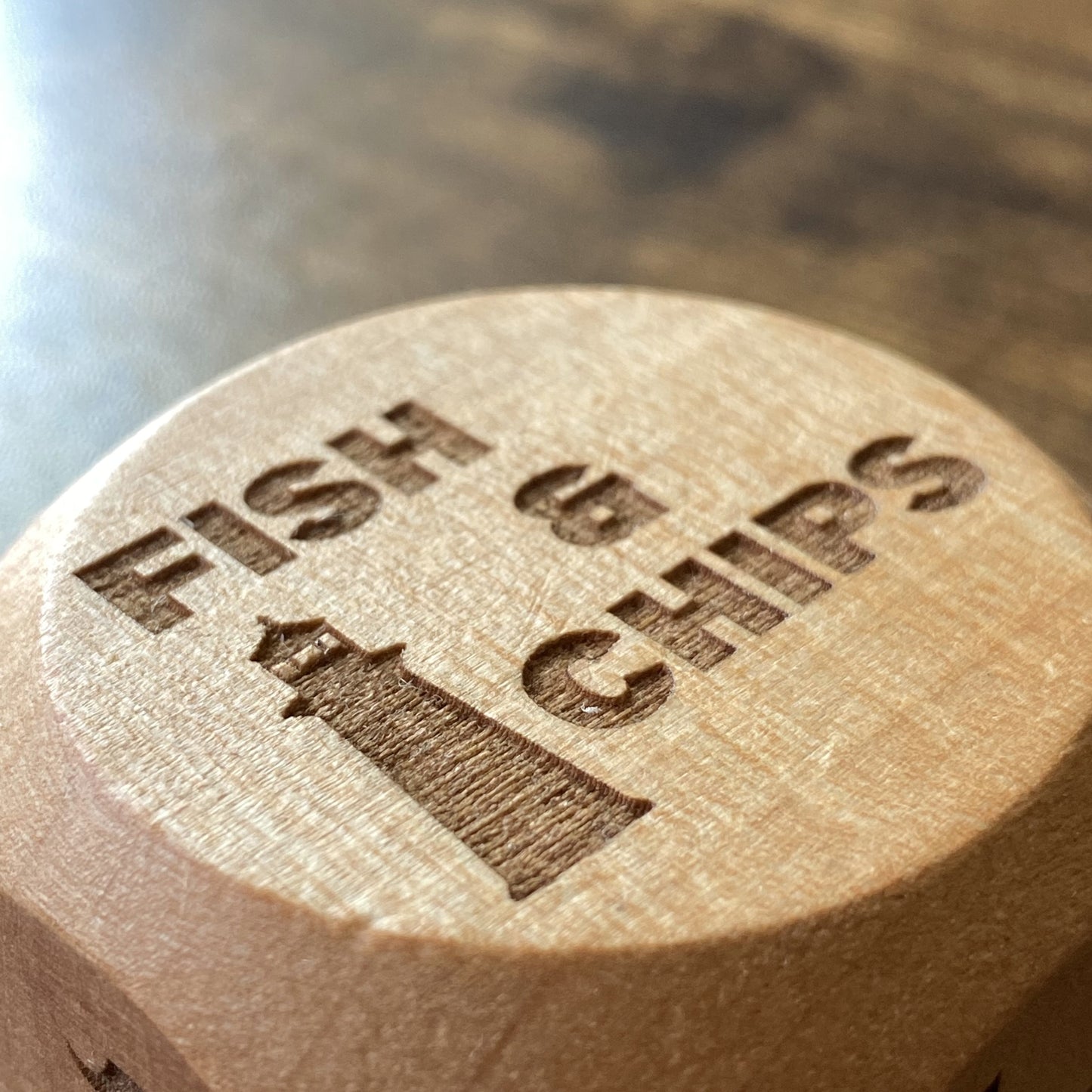 Close-up of Takeout Decision Dice showing 'Fish & Chips' engraving on smooth wooden dice face