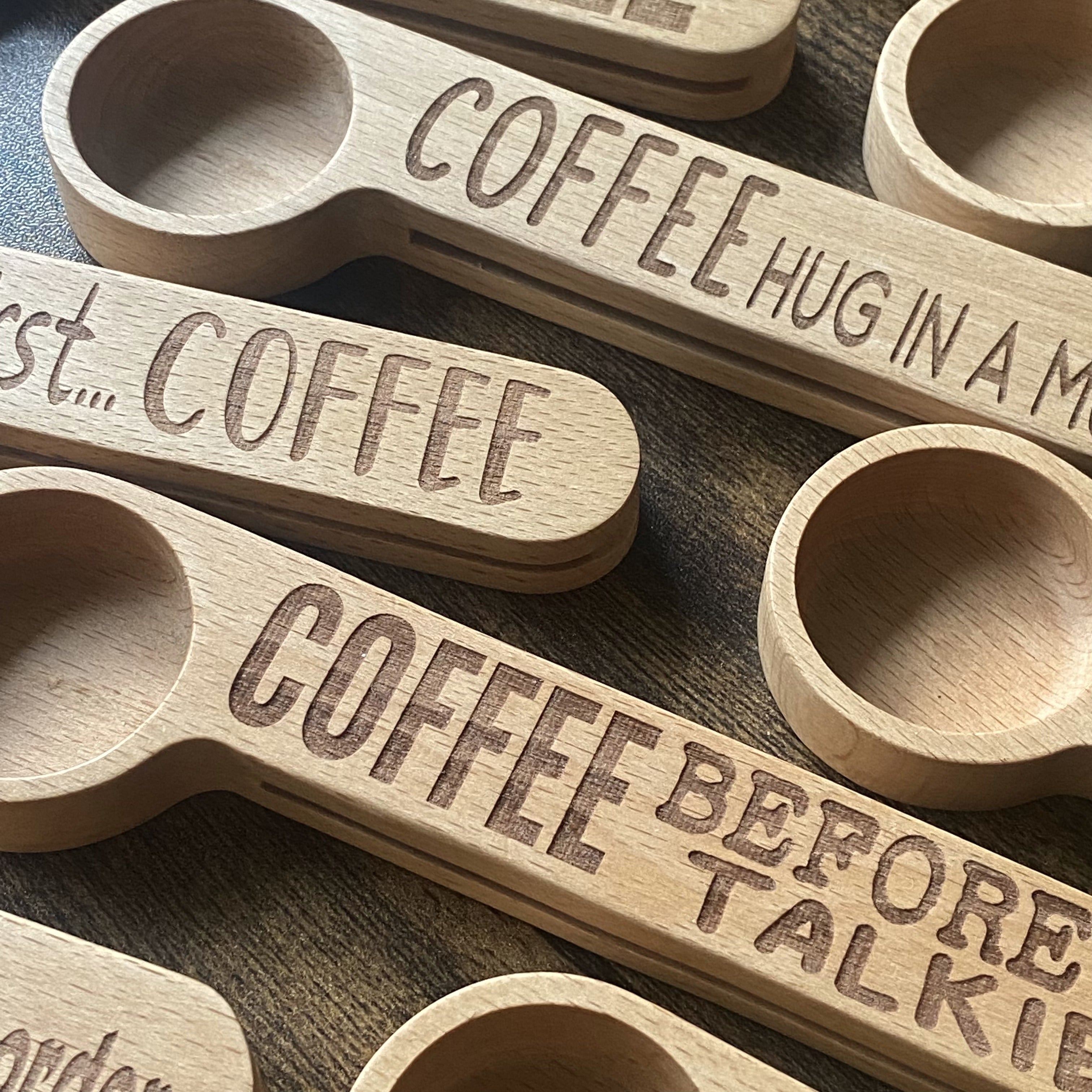 A close-up shot of scattered wooden coffee spoons, each engraved with a witty coffee quote, highlighting the intricate design and craftsmanship of each piece.