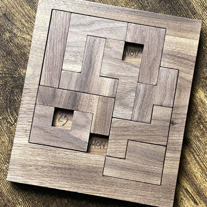 Top-down angled view of walnut wooden calendar puzzle with square pieces and fine engraved detailing