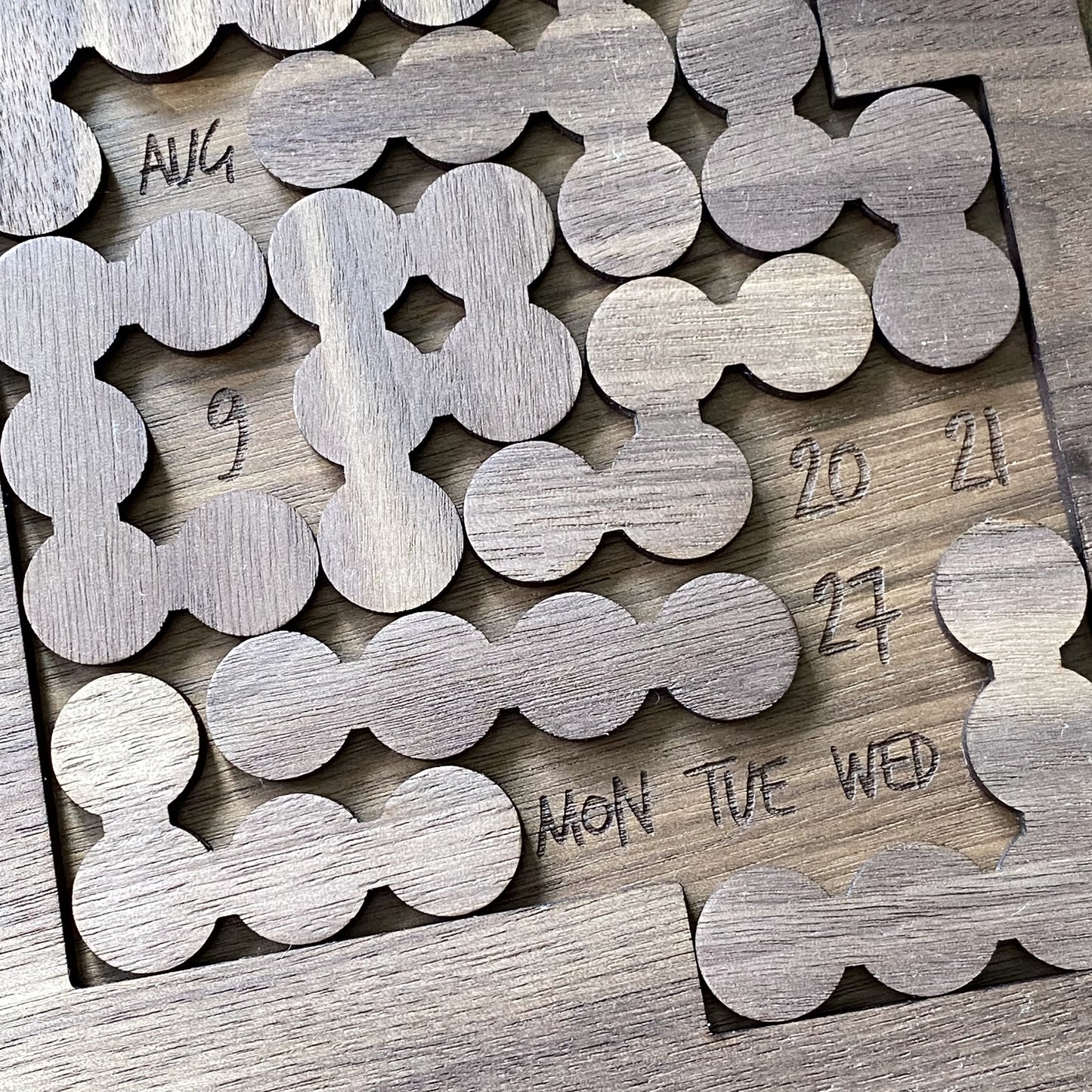 Top-down view of walnut bubble pieces from the Daily Perpetual Calendar Puzzle, showing natural wood grain and engraved detail."