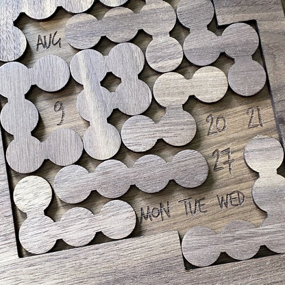 Top-down view of walnut bubble pieces from the Daily Perpetual Calendar Puzzle, showing natural wood grain and engraved detail."