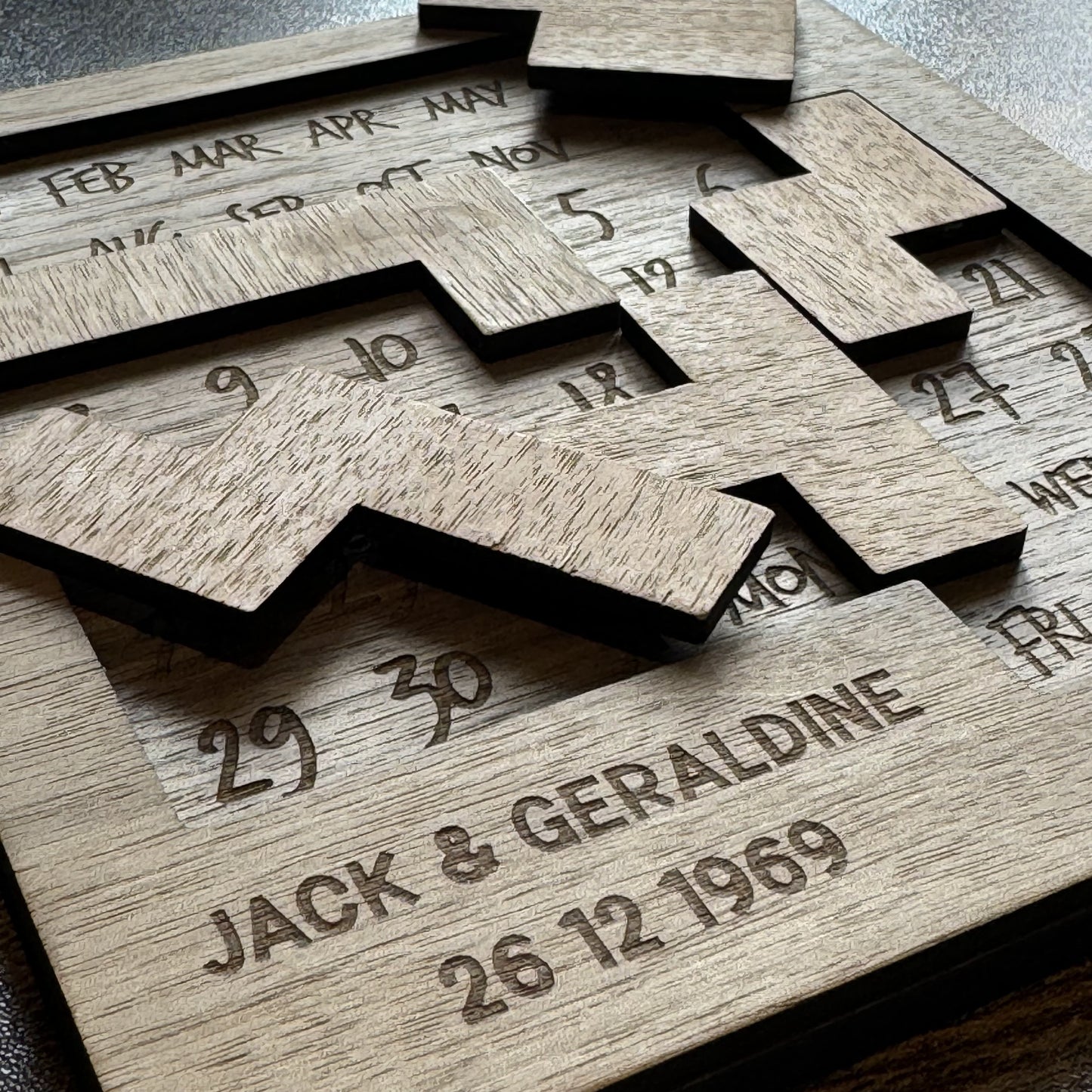 Scattered walnut puzzle pieces on engraved calendar board with personalised detail