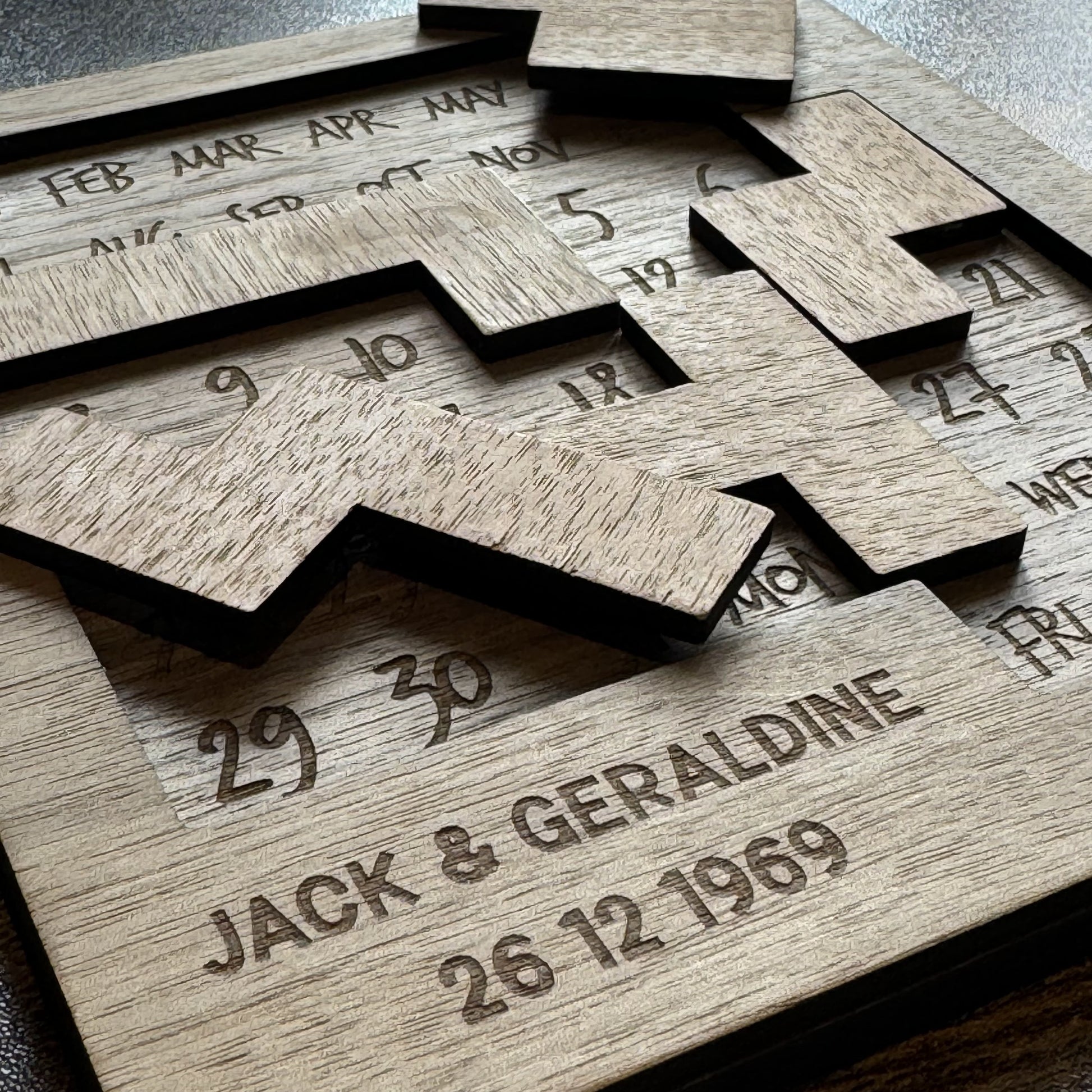 Scattered walnut puzzle pieces on engraved calendar board with personalised detail