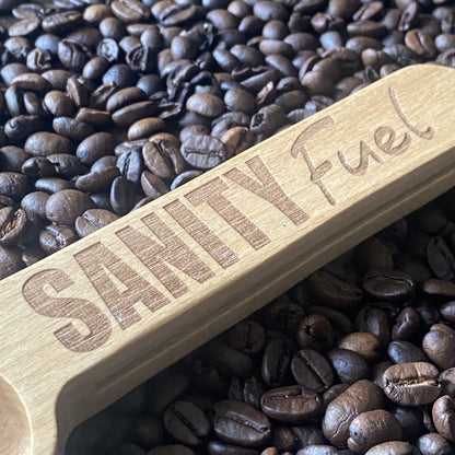 Close-up of the wooden coffee scoop resting on a bed of coffee beans, highlighting the engraved details and smooth finish.