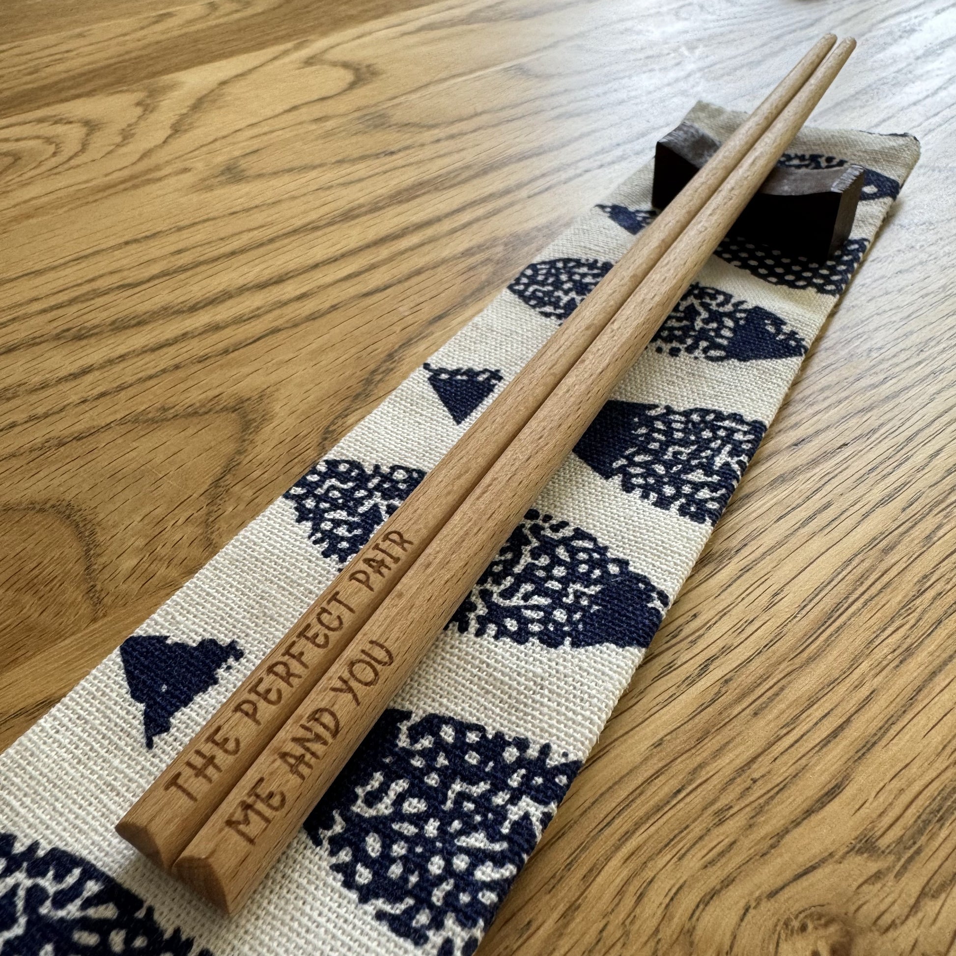 The Perfect Pair / Me and You” bamboo chopsticks resting on pouch and wooden stand, viewed along chopstick pair.