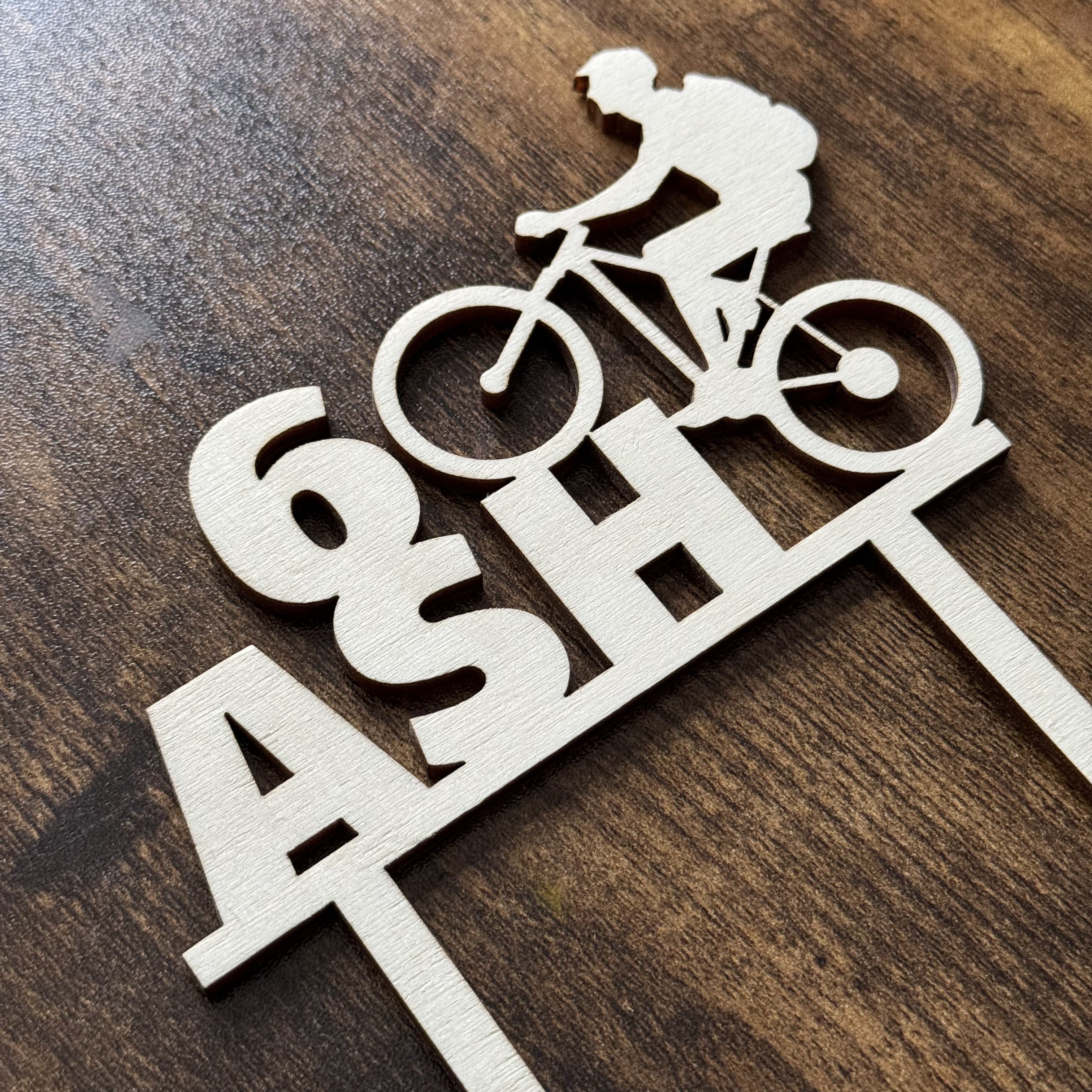 Custom wooden cake topper featuring a mountain biking silhouette interlinked with a birthday number, designed for active lifestyle celebrations
