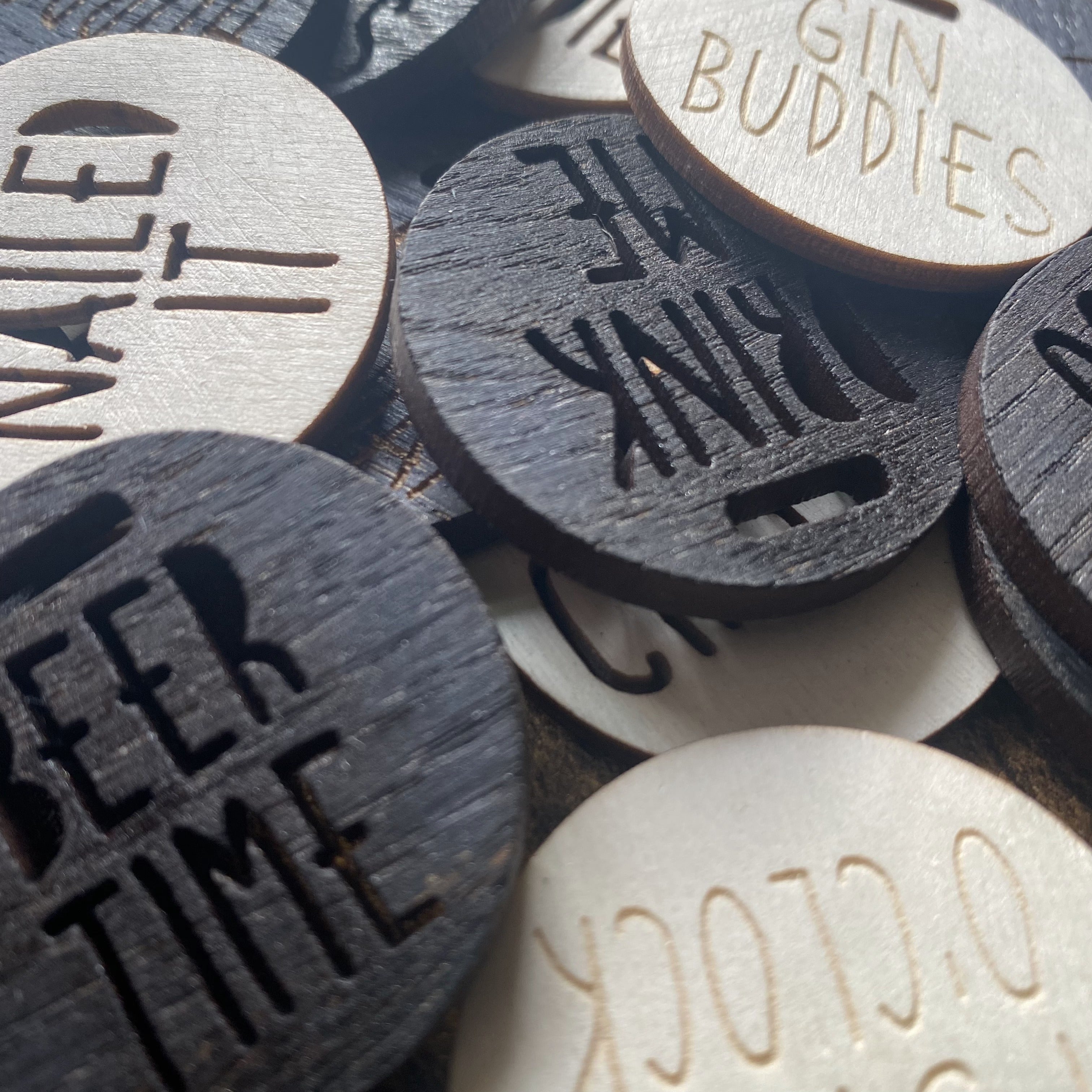 Close-up of a pile of engraved wooden bottle charms showing varied messages and finishes