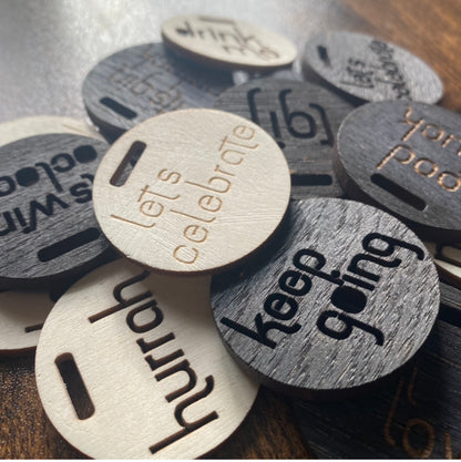 Scattered pile of wooden engraved bottle charms photographed at an angle – ideal for gifting and celebrations