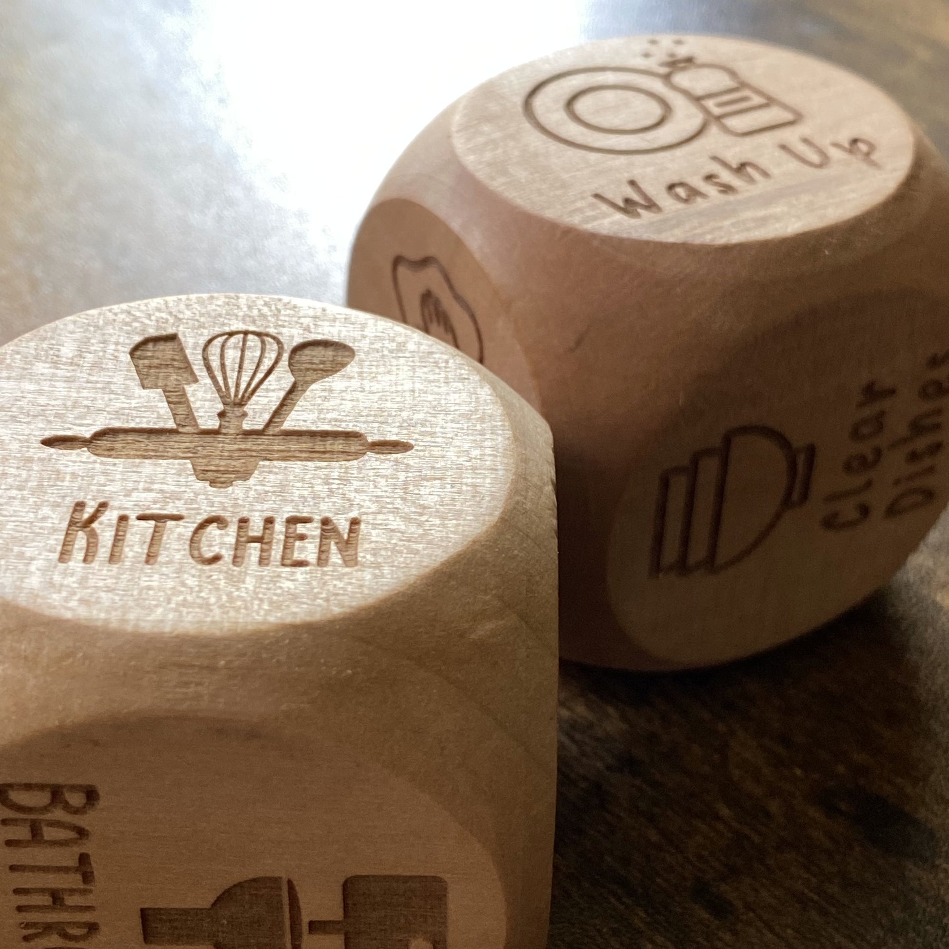 Close-up of two engraved wooden dice - Junior Chores and Household Chores - showing detailed task engravings and natural wood grain