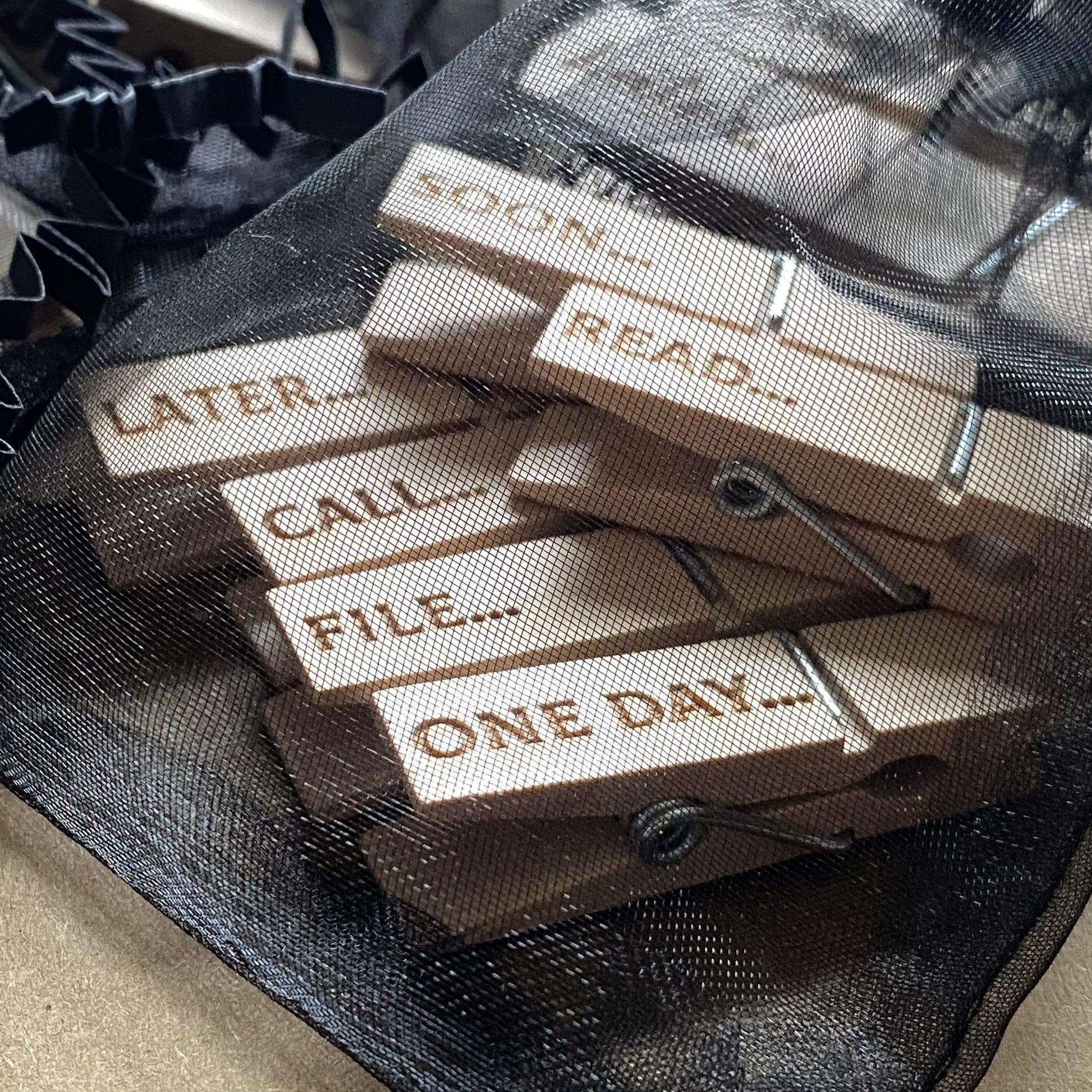 Soft organza bag open to reveal six natural wood mini desk organisation pegs inside, engraved with playful designs, perfect for tidy desk organisation.