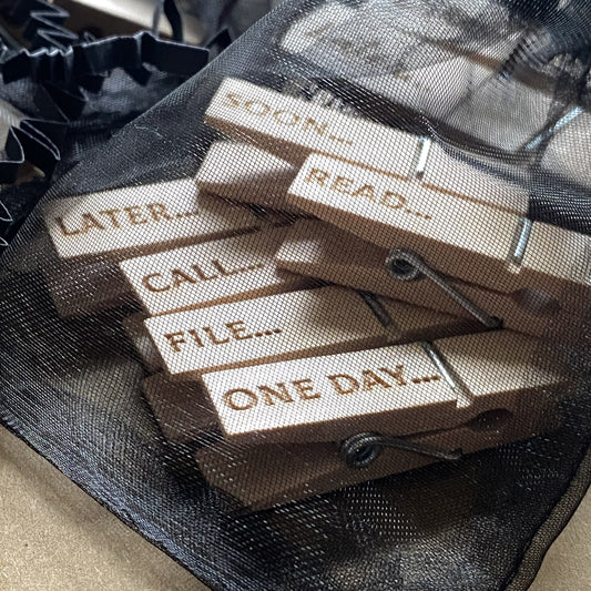 Soft organza bag open to reveal six natural wood mini desk organisation pegs inside, engraved with playful designs, perfect for tidy desk organisation.