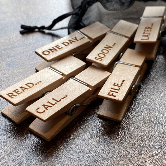 Six natural wood mini desk organisation pegs scattered from a soft organza bag on a wooden surface, showing charming engraved designs and tidy workspace vibes.