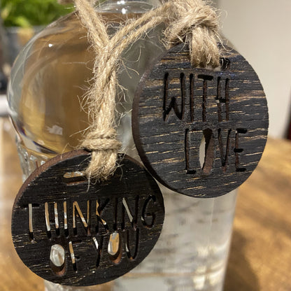 Close-up of two engraved wooden charms on a gin bottle, featuring ‘With Love’ and ‘Thinking of You’ cut-out lettering on blackened oak