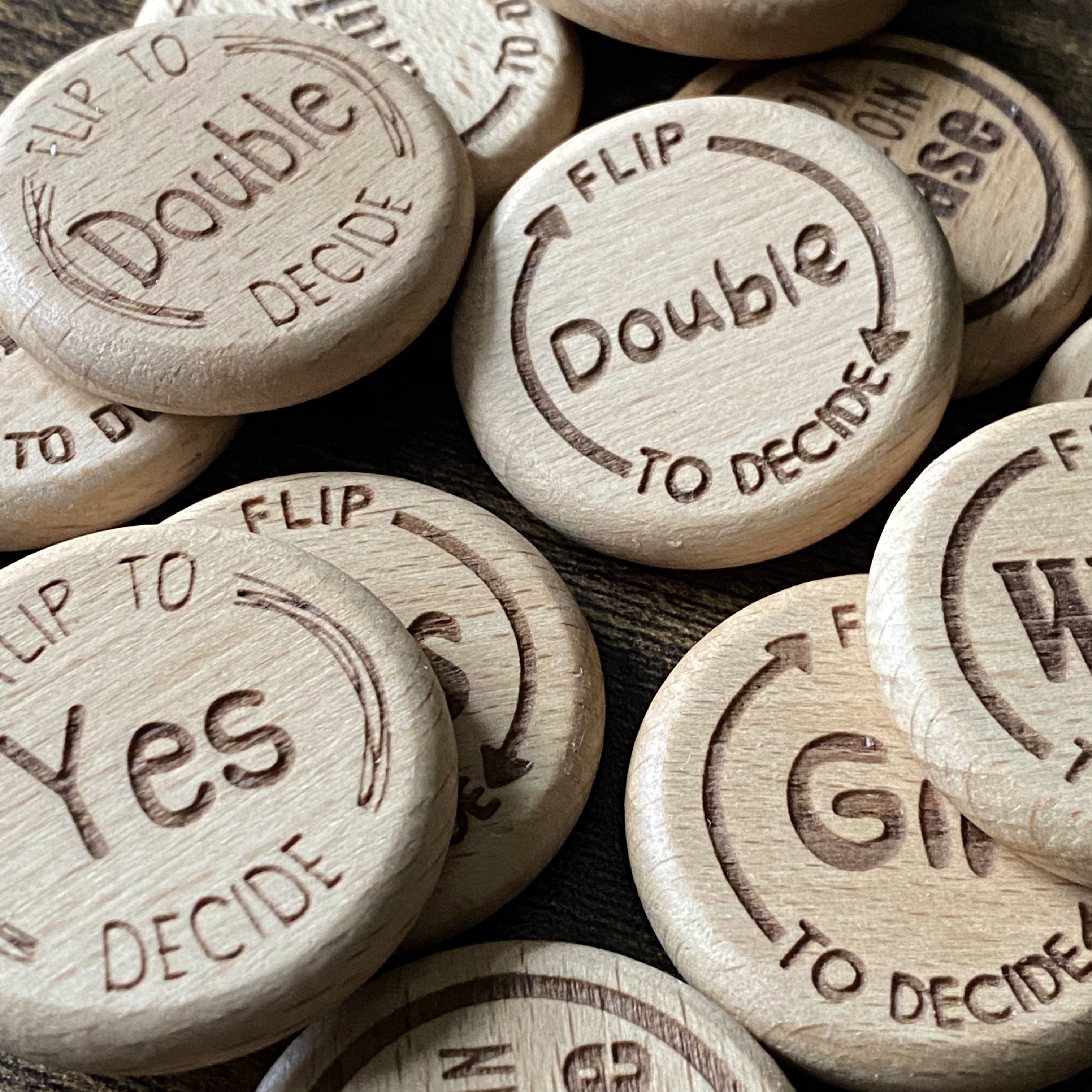Mixed pile of Friday Night Drinking Trio Flip Coins in all four designs, showcasing the variety of engraved wooden styles