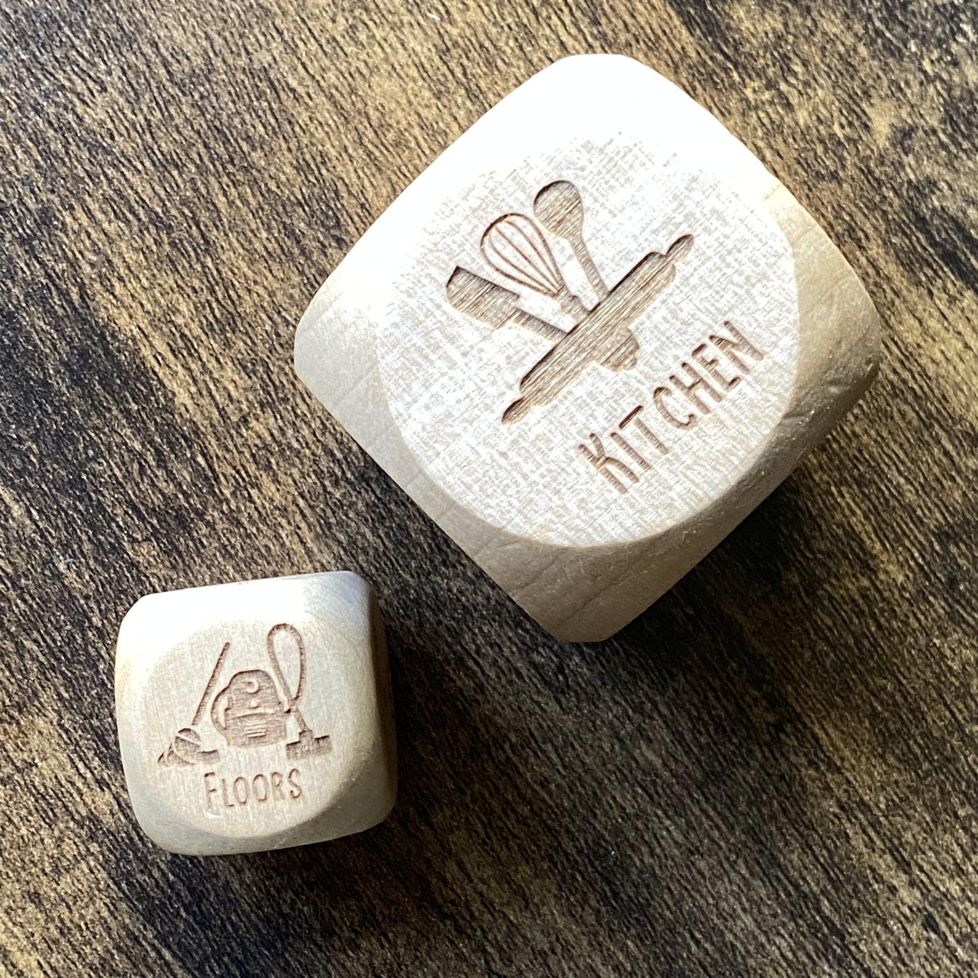 Top-down view of two sizes of engraved wooden Household Chores Decision Dice set side by side, showing detailed task engravings and smooth finish