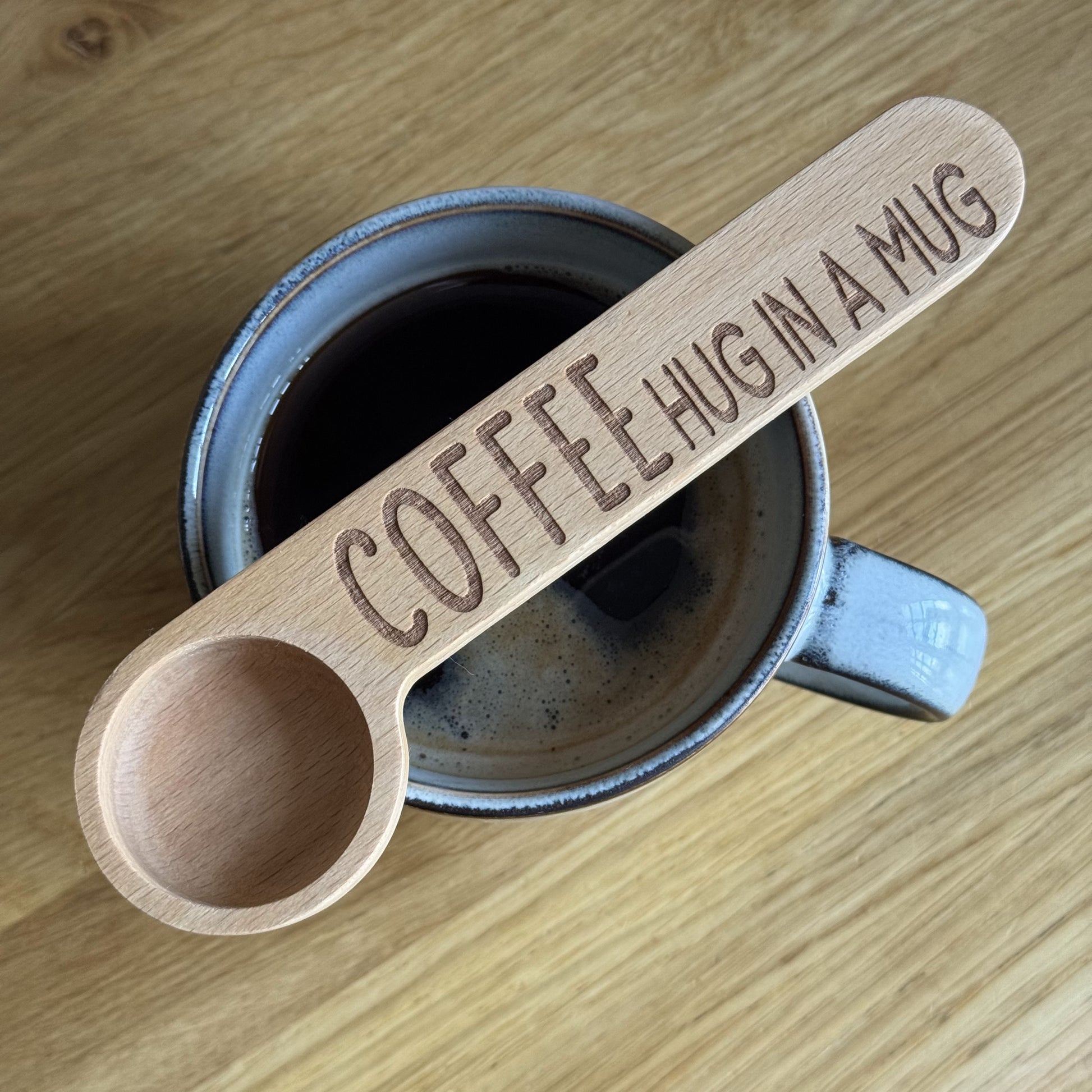 Top-down view of a mug with a Hug in a Mug engraved coffee spoon resting across the top
