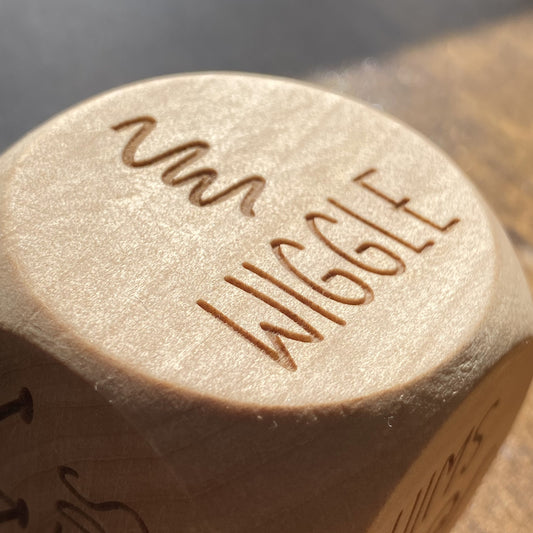 Close-up detail of "wiggle" engraved on a wooden Junior Exercise Decision Dice, with clear playful illustration
