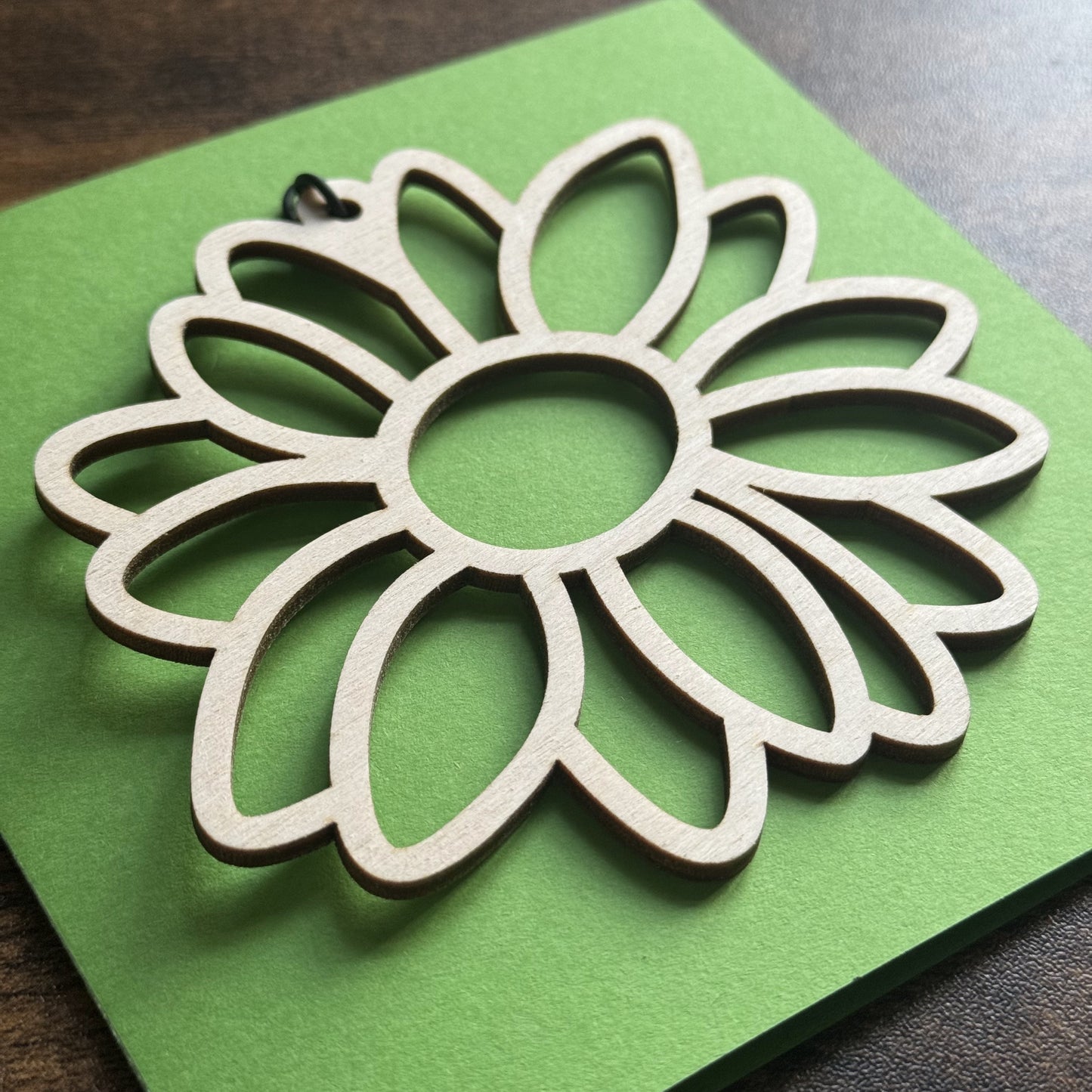 Angled view of Keepsake Charm Card featuring a delicate wooden gerbera flower charm with matching ribbon, naturally lit.