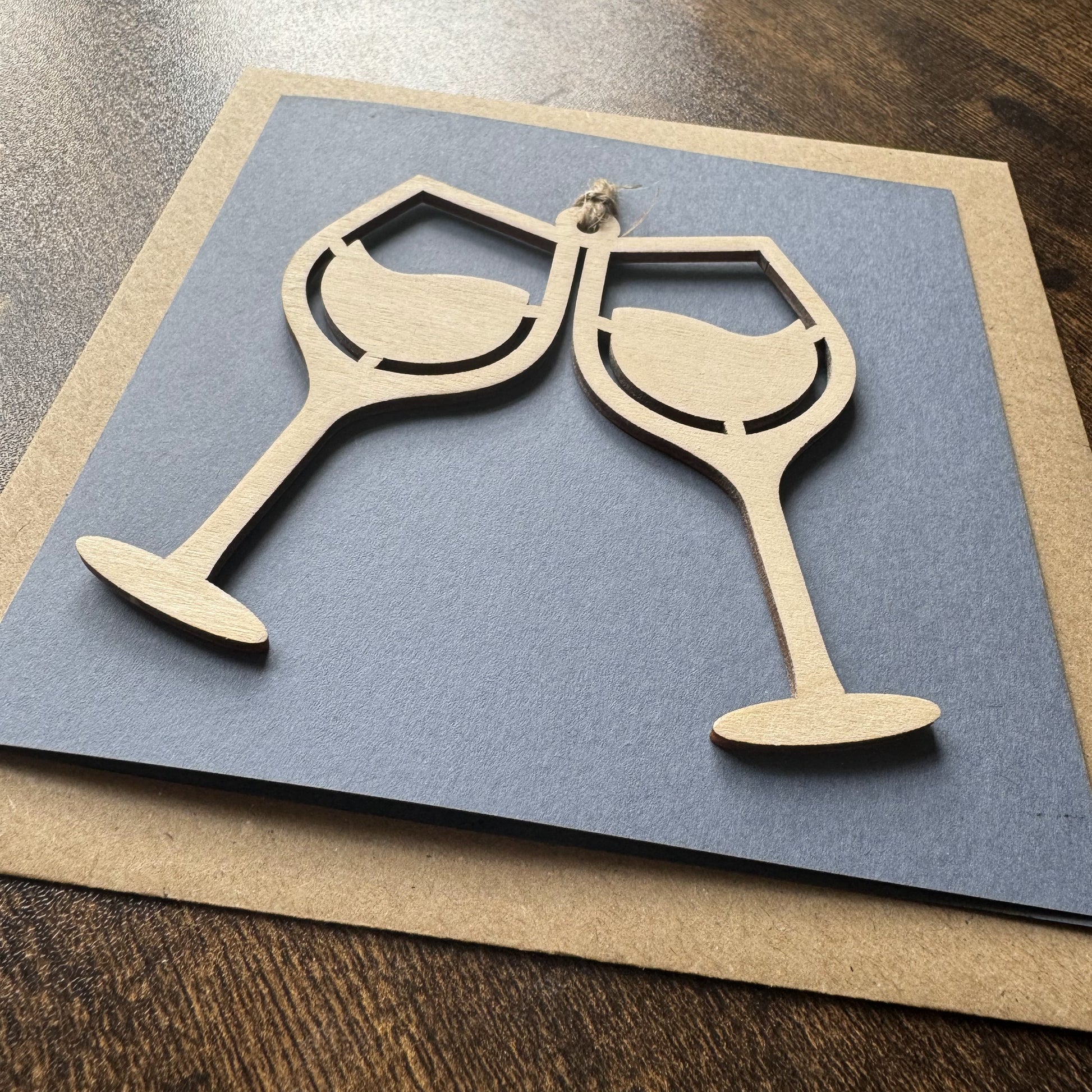 Angled view of Keepsake Charm Card featuring a charming wooden wine glasses design with coordinating ribbon, presented with kraft envelope