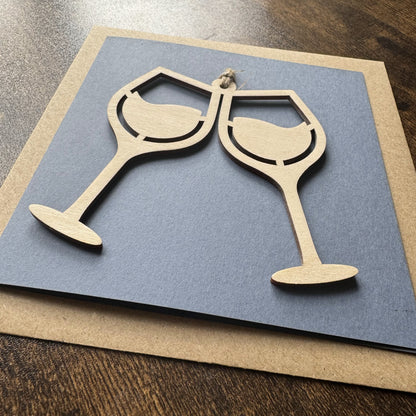 Angled view of Keepsake Charm Card featuring a charming wooden wine glasses design with coordinating ribbon, presented with kraft envelope
