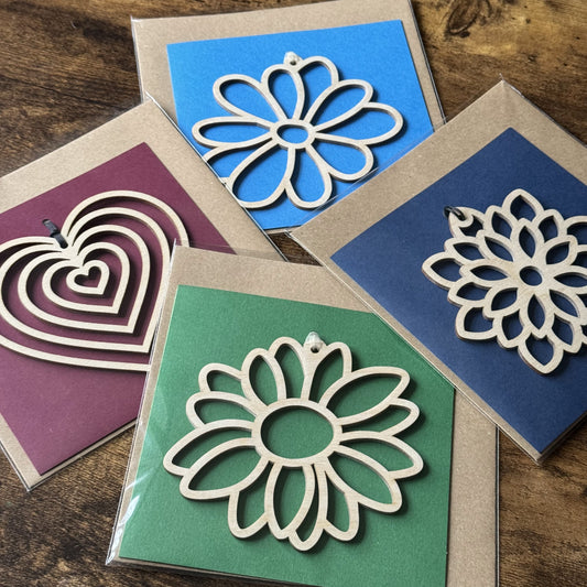 Four Keepsake Charm Cards scattered in their packaging, each featuring different wooden charms and coordinated ribbons, for a stylish, gift-ready presentation.