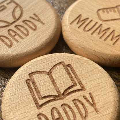 Close-up of the solid wood New Baby Duties Flip Coins, highlighting their tactile texture and engraved wording combinations