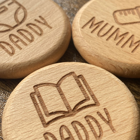Close-up of the solid wood New Baby Duties Flip Coins, highlighting their tactile texture and engraved wording combinations