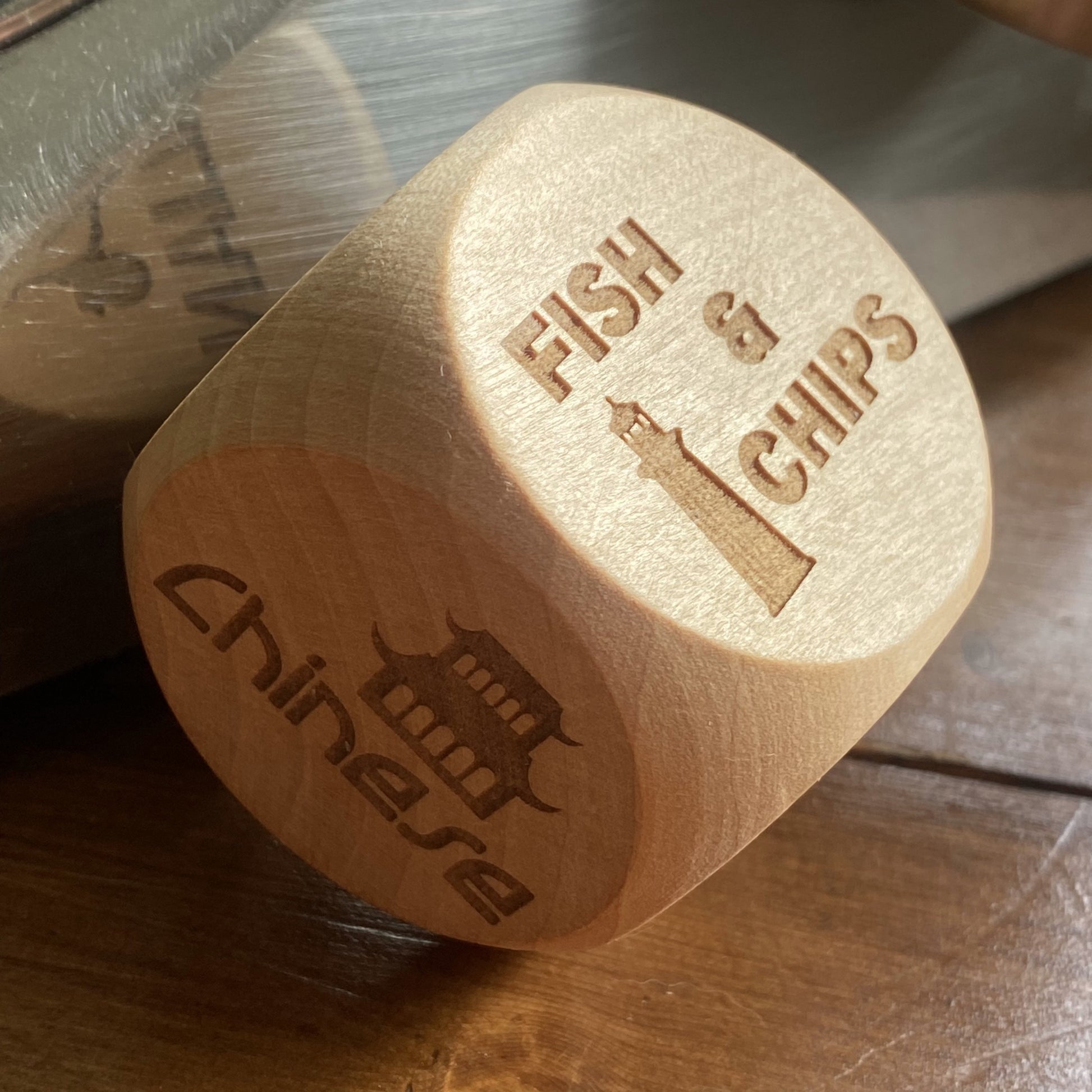 Angled shot of Takeout Decision Dice with 'Fish & Chips' engraving on a home wooden table