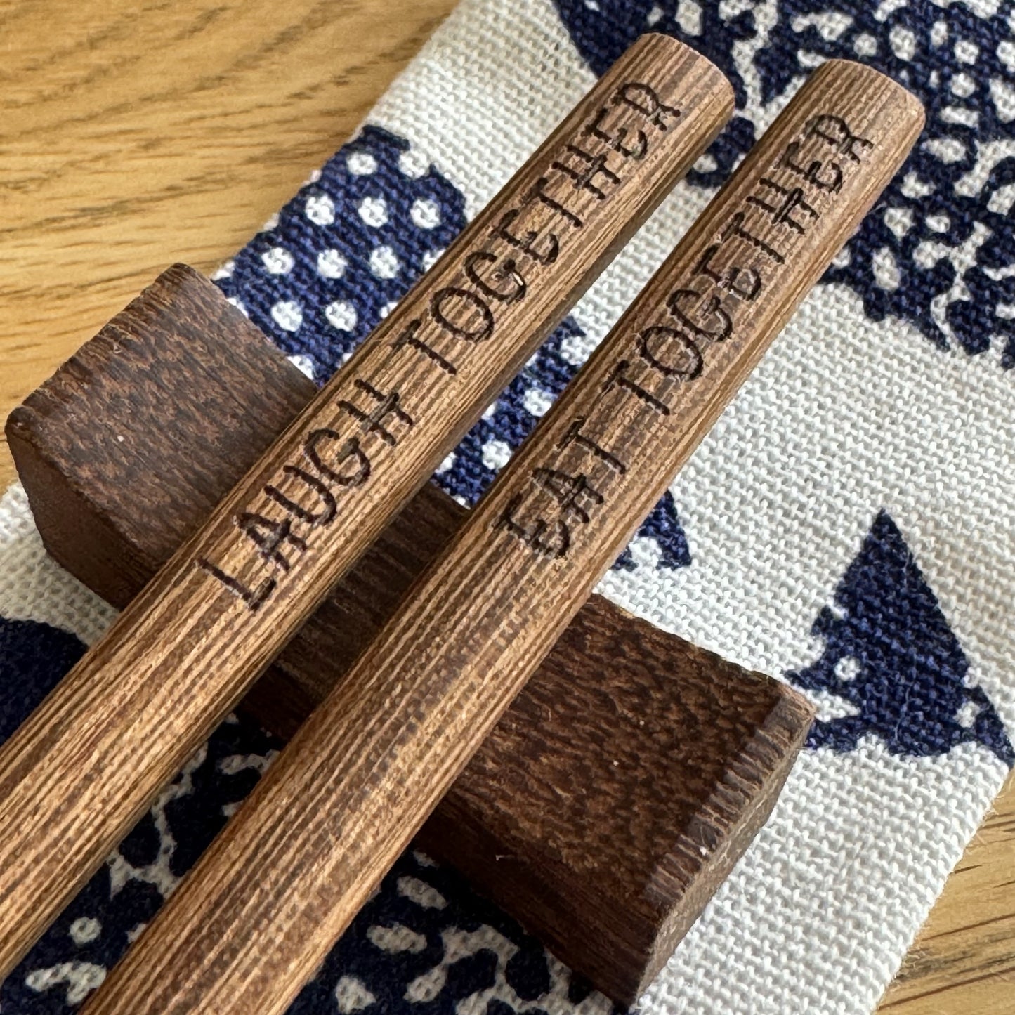 Wenge chopsticks engraved with “Laugh Together, Eat Together” on stand, with pouch behind.