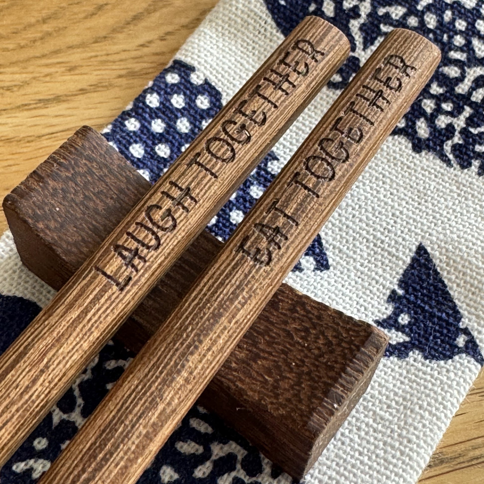 Wenge chopsticks engraved with “Laugh Together, Eat Together” on stand, with pouch behind.