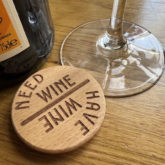Wooden tipple spinner with 'Need wine, Have wine' design next to a wine glass and bottle on a wooden surface
