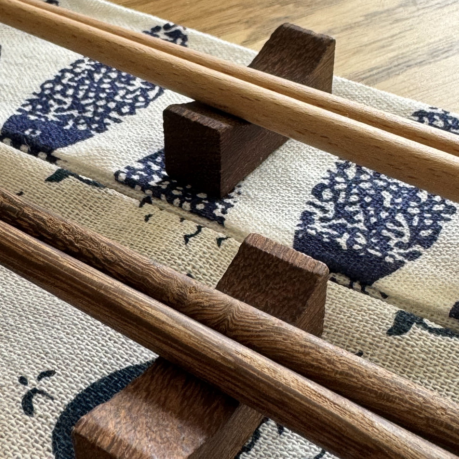 Bamboo and wenge chopsticks balanced on rest and pouch, highlighting wood variation.